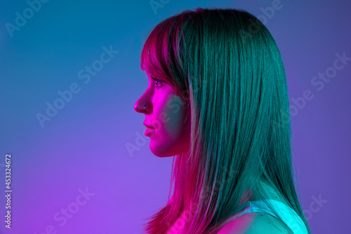 Close-up portrait of young beautiful girl isolated on blue studio background in neon light filter. Concept of human emotions, facial expression, youth, sales, ad.