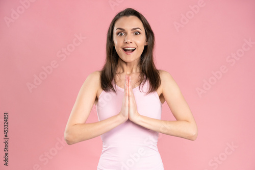 Portrait of pretty young woman wearing pink t-shirt begging or praying with hands together, hope and joy expression on her face with positive emotions.