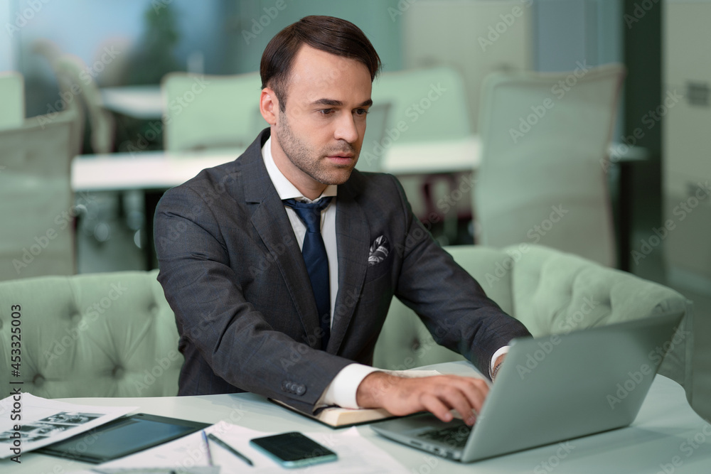 Freelancer sitting in front laptop in bright coworking space. Handsome man in business suit working on laptop, freelancer job in progress. Freelancer sitting in front laptop in bright coworking space. Handsome man in business suit working on laptop, freelancer job in progress.