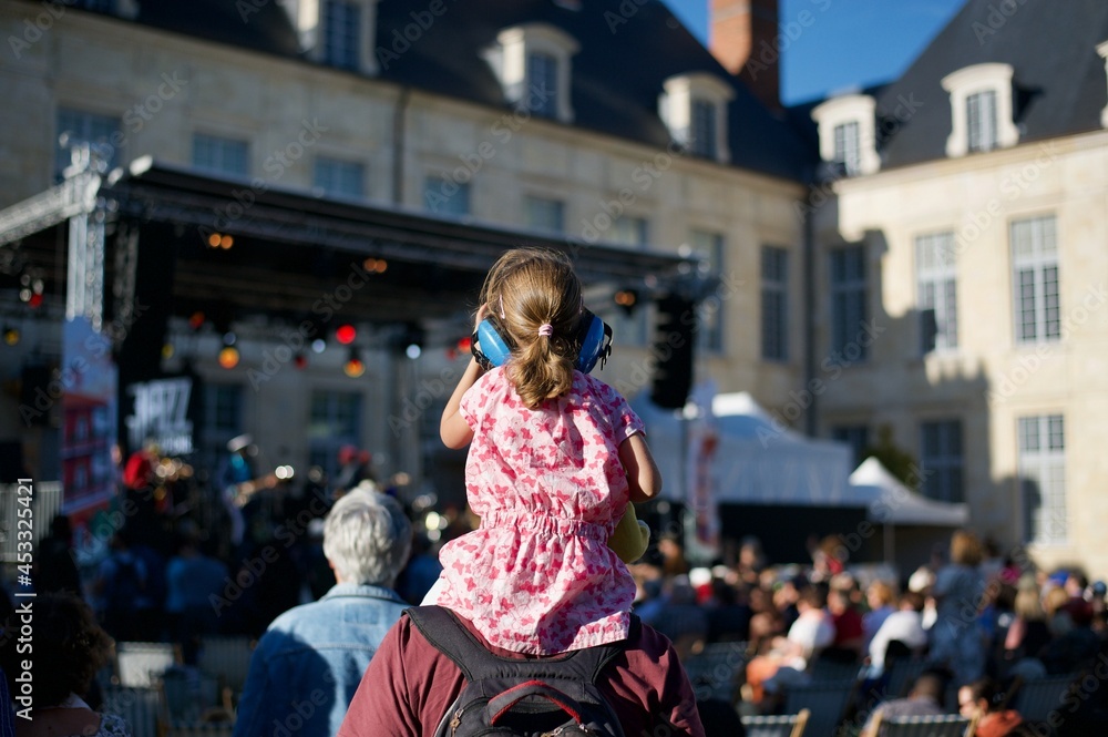 Fototapeta premium a young girl on shoulders of his father is wearing hearing protection helmet and is attending a live music show