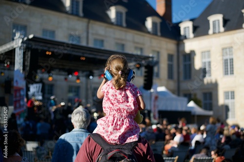 a young girl on shoulders of his father is wearing hearing protection helmet and is attending a live music show