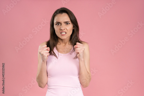 Showing ager beautiful young woman wearing pink t-shirt holding hands gathered in fists  Female half-length portrait. Human emotions  facial expression concept.