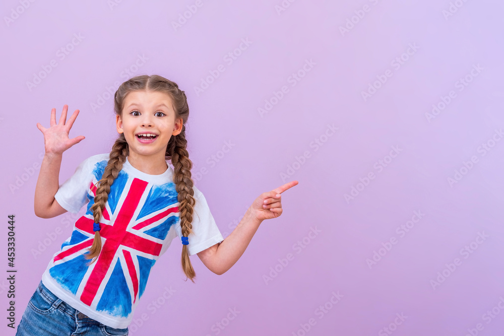 A child in a shirt with a British flag points to your ad on an isolated pink background. - obrazy, fototapety, plakaty 