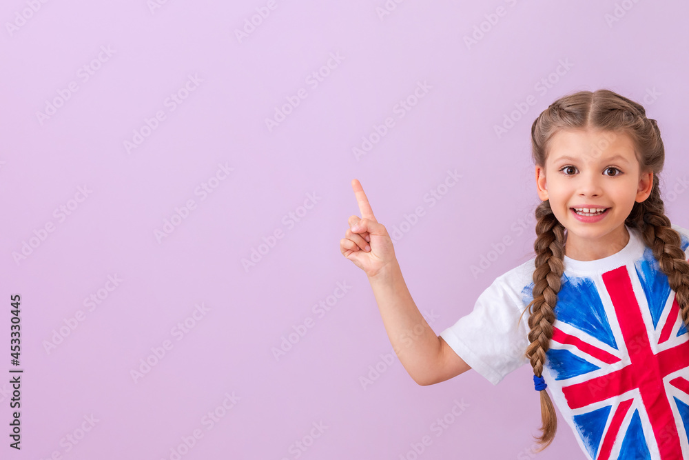 A child in a shirt with a British flag points to your ad on an isolated pink background. - obrazy, fototapety, plakaty 