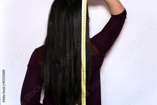Mujer morena sosteniendo una cinta métrica amarilla para medir la longitud de su cabello largo y negro photo