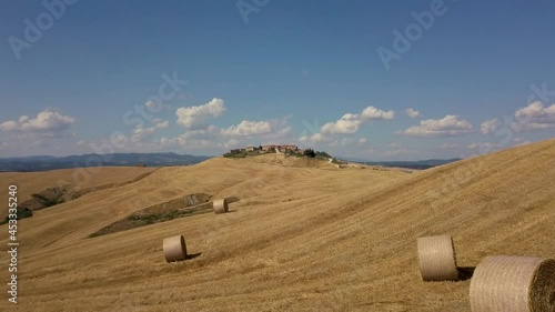 Aerial Drone Golden Hay harvest in the Arbia valley south of Siena Tuscany on a sunny summer day with clouds in the sky and medieval old town in the background - flying close to hay bales photo