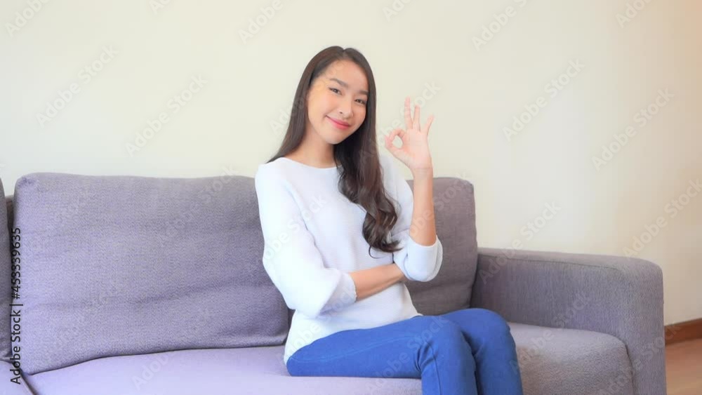 Asian Woman on Couch Makes the OK Sign with Thumb and Index Finger. Asian Woman on Couch Makes the OK Sign with Thumb and Index Finger.
