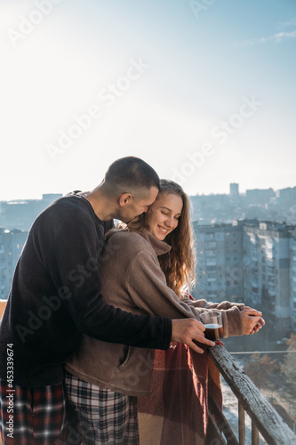 Young couple drinking coffee on the balcony of the apartment in the morning. Young happy couple, newlyweds family start new day and have morning coffee together