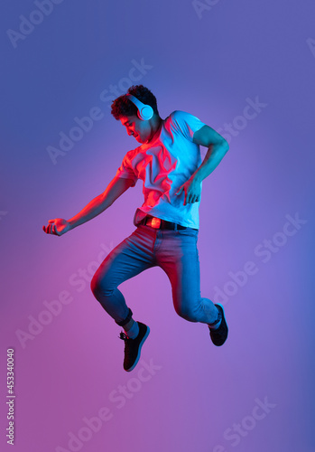 Stylish young asian man jumping isolated over lilac color studio background in pink neon light. Concept of human emotions, fashion, beauty, youth
