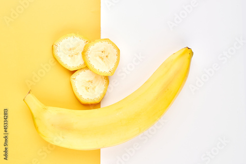 Banana creative background. Yellow and white backdrop with whole, peeled, sliced bananas