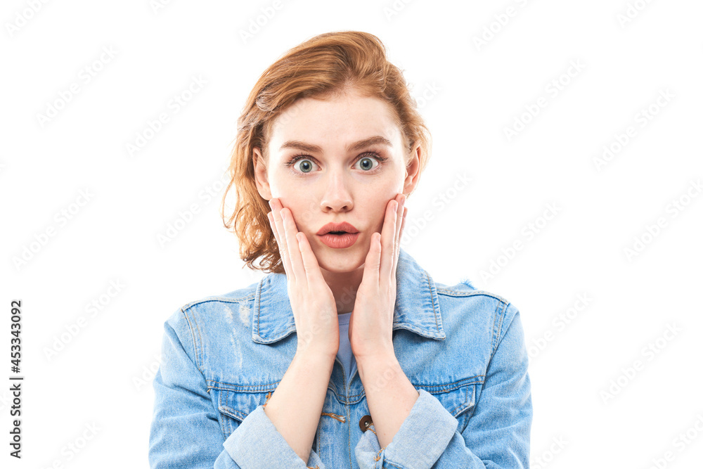 Young red-haired woman is surprised with her mouth wide open. Shocked girl in jeans on a white background looks at the camera Young red-haired woman is surprised with her mouth wide open. Shocked girl in jeans on a white background looks at the camera