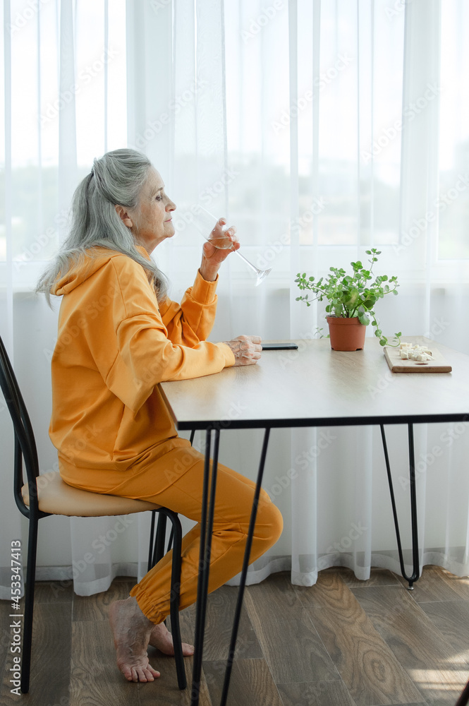 Beautiful old grandmother with grey hair and face with wrinkles is using smartphone, talking with someone and sitting at the table at home on window background, mother's day, happy retirement Beautiful old grandmother with grey hair and face with wrinkles is using smartphone, talking with someone and sitting at the table at home on window background, mother's day, happy retirement