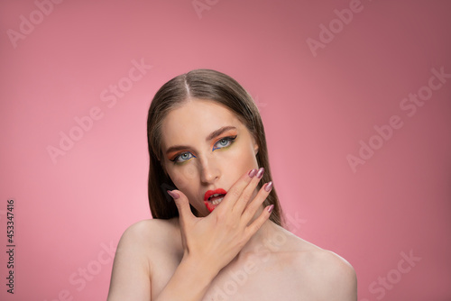 Messing up lipstick on face fashion model beautiful woman with long straight hair standing in the studio isolated on dirty pink background. Lips make up concept. 