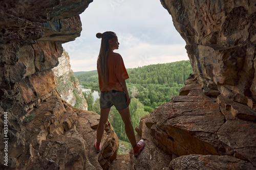 Silhouette of a girl with long dreadlocks who stands inside a cave overlooking the green forest. The concept of travel and freedom. High quality photo