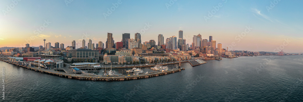 Fototapeta premium Aerial panoramic view of Seattle, Washington. Skyscrapers can be seen with a sunset along with an ocean bay with boats. 