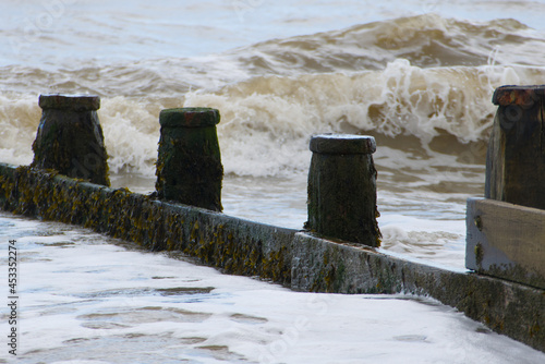 Waves crashing onto the weathered wooden groyne as the tide comes in at Frinton-on-Sea, Essex, UK. photo