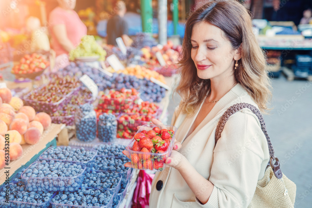 Middle age stylish pregnant woman enjoy shoping, shoosing berries, holding shopping net bag in eco friendly farmer market. Low waste, plastic free lifestyle concept. Eco reusable shopper outdoors. Middle age stylish pregnant woman enjoy shoping, shoosing berries, holding shopping net bag in eco friendly farmer market. Low waste, plastic free lifestyle concept. Eco reusable shopper outdoors.