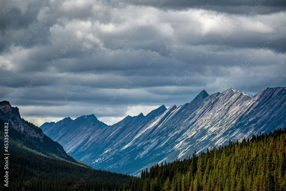 Obraz premium THE ENDLESS CHAIN UNDER OVERCAST DARK CLOUDS WITH SUN ON PEAKS AND PINES - JASPER NP