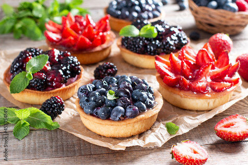 Strawberries, blueberries, blackberries tartlets with chocolate ganache, fresh berries and mint leaves. Fresh fruit tart, freshly homemade fruit cake on a table