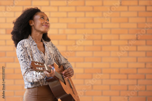 Woman playing guitar outside looking up on a brick wall background