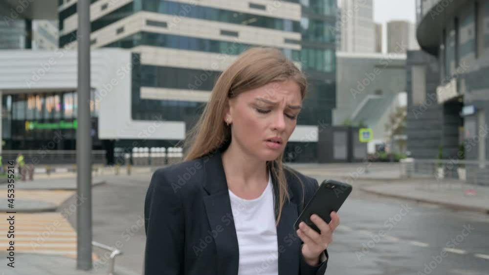 Young Businesswoman Reacting to Loss on Smartphone while Walking on the Street Young Businesswoman Reacting to Loss on Smartphone while Walking on the Street