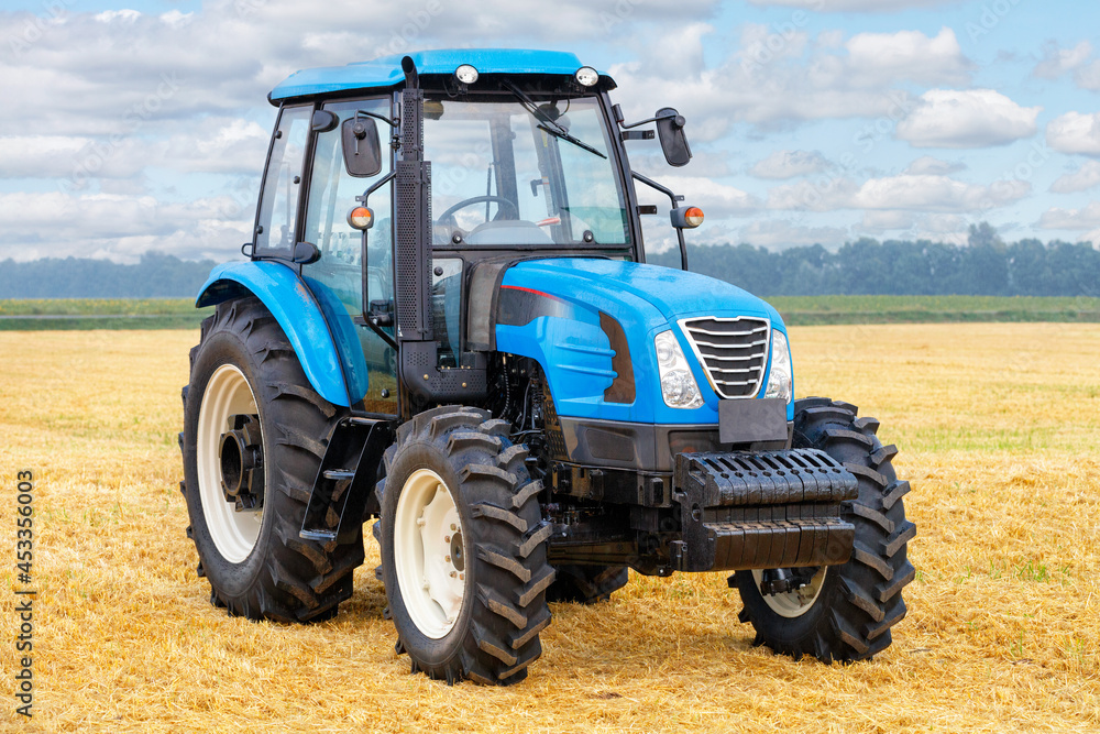 Wheeled farm tractor with harvested yellow wheat field and cloudy sky in the background. Wheeled farm tractor with harvested yellow wheat field and cloudy sky in the background.