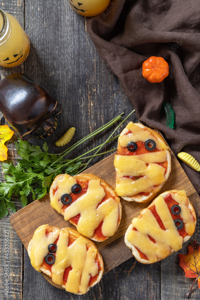 Halloween party food. Halloween mummies mini pizzas on a wooden table. Top view flat lay background. Copy space.
