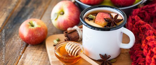 Homemade hot fruit tea with fresh apples, honey, spices: cinnamon, cardamon, anise, clove. Warm autumn drink, delicious healthy beverage. Mulled wine. Cozy home atmosphere. Wooden background. Banner