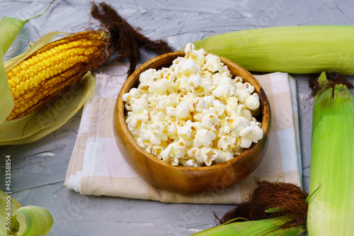 A bowl with delicious traditional popcorn and corn cobs on a gray background