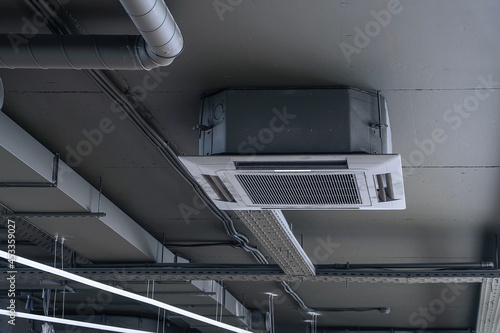 Cassette split system on gray ceiling with ventilation ducts. Indoor unit of air conditioner. Engineering air system.