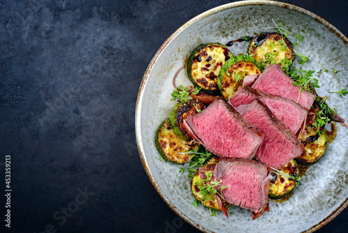 Modern style traditional fried dry aged angus beef filet medaillons with zucchini and cress served in a Nordic design bowl with copy space left