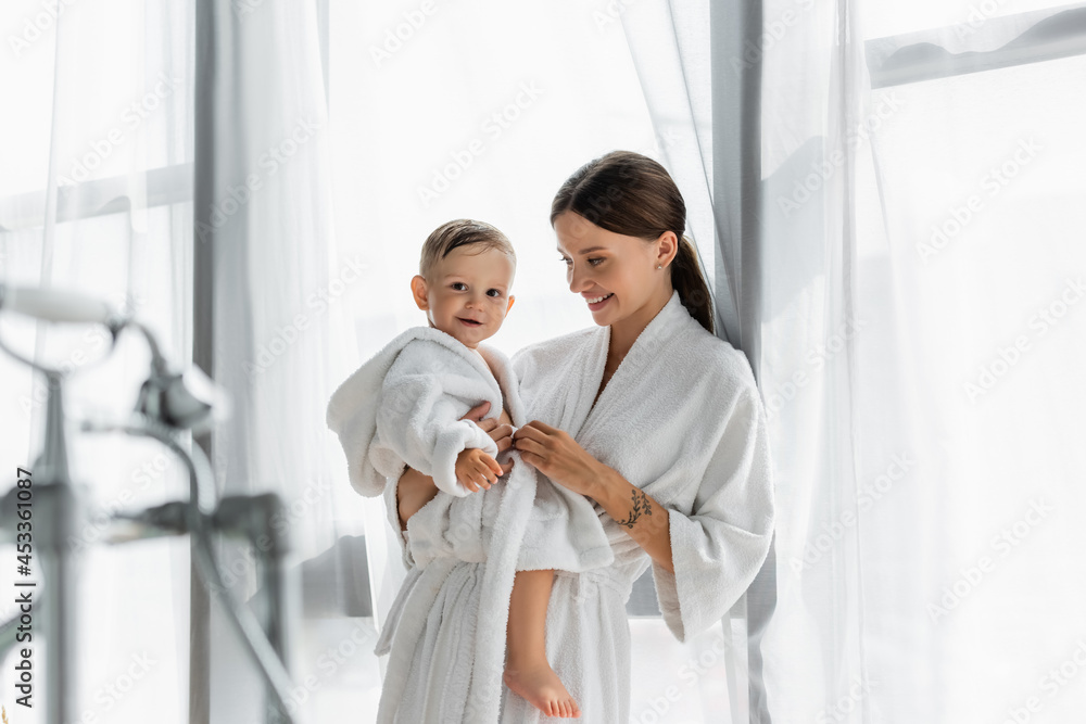 cheerful mother looking at toddler son in bathrobe cheerful mother looking at toddler son in bathrobe
