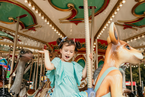 A cheerful little girl in a blue dress rides on an amusement park ride