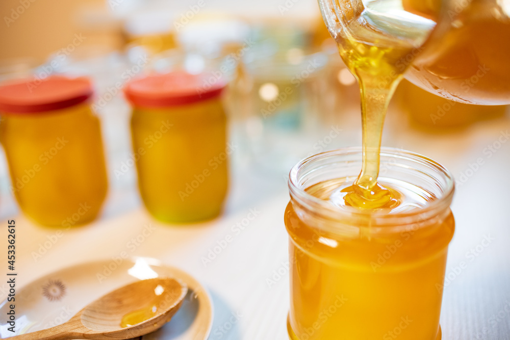 Someone pours honey into transparent jars on a white table Someone pours honey into transparent jars on a white table