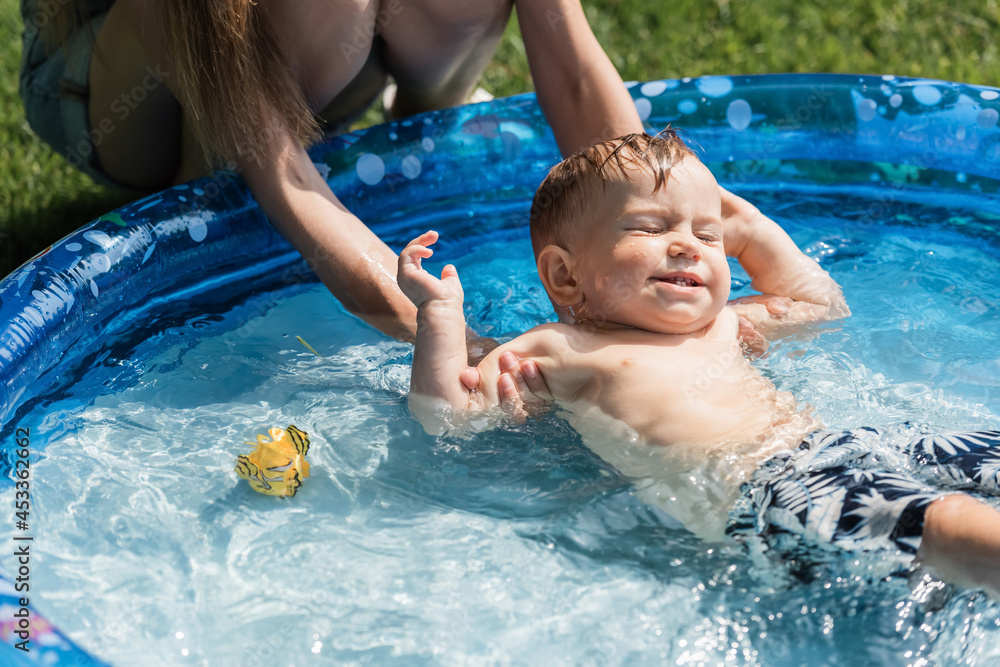 mother bathing shirtless toddler son with closed eyes in inflatable pool mother bathing shirtless toddler son with closed eyes in inflatable pool