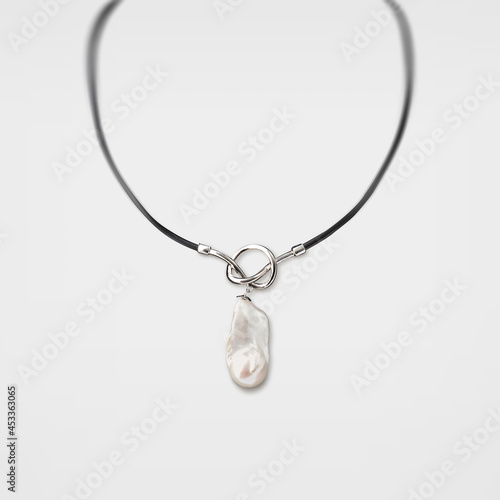 Silver necklace with pretzel loop and uncut pearl pendant on gray background