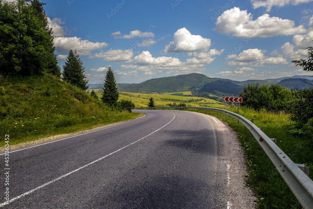 Asphalt road in mountain hilly countryside in pine forests, on background of blue sky with clouds, Ukraine, Carpathians