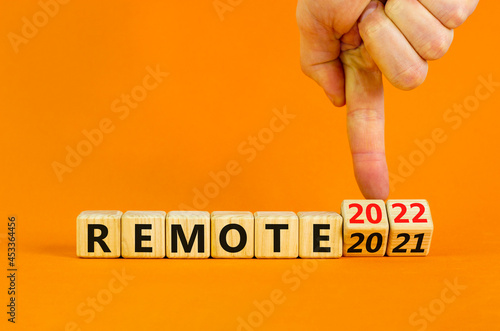 Planning 2022 remote new year symbol. Businessman turns wooden cubes and changes words 'remote 2021' to 'remote 2022'. Beautiful orange background, copy space. Business, 2022 remote new year concept.