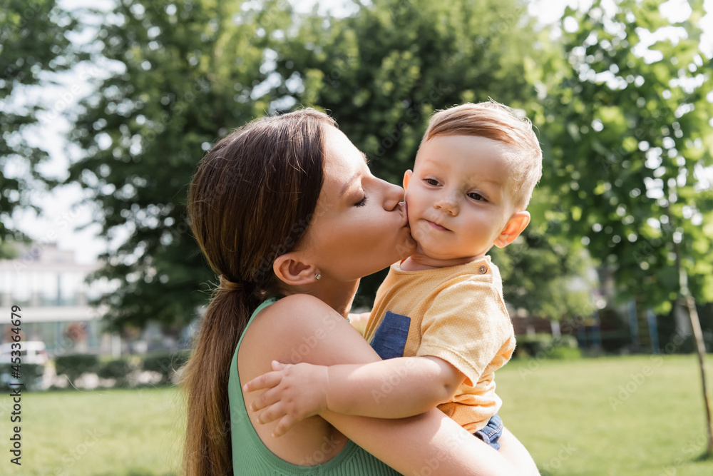 young mother holding in arms and kissing toddler son young mother holding in arms and kissing toddler son