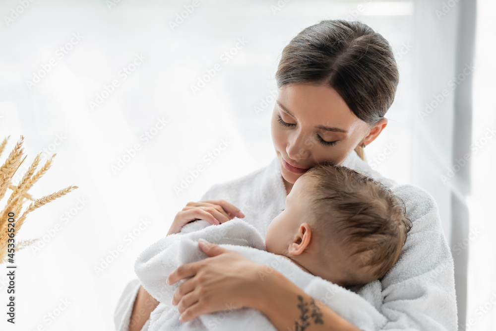 caring mother hugging toddler son with closed eyes in bathrobe caring mother hugging toddler son with closed eyes in bathrobe