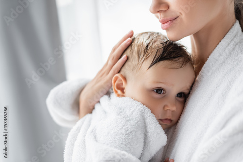 pleased young mother holding in arms toddler son in bathrobe