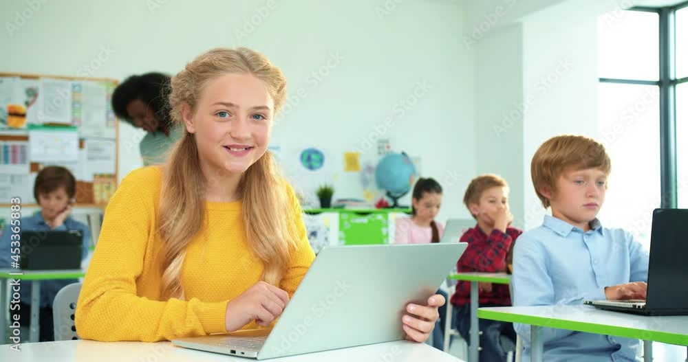 Kids learning in elementary school Close up portrait of Caucasian happy schoolgirl typing on laptop browsing online at computer science class African American female teacher using tablet on background Kids learning in elementary school Close up portrait of Caucasian happy schoolgirl typing on laptop browsing online at computer science class African American female teacher using tablet on background