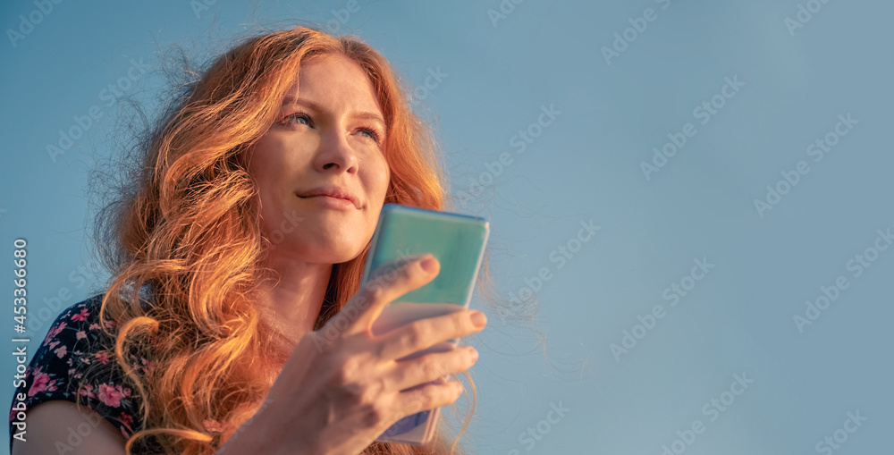 Pretty nice ginger lady in summer dress using smartphone in front of the sky Pretty nice ginger lady in summer dress using smartphone in front of the sky