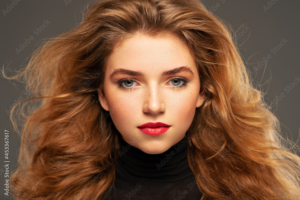 Closeup portrait of an young adult girl with long curly hair.  Photo of a fashion model posing at studio. Pretty young woman with red lips looking at camera. Beauty portrait.