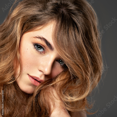 Closeup portrait of an young adult girl with long curly hair.  Photo of a fashion model posing at studio. Pretty young woman with long brown hair looking at camera. Beauty portrait.