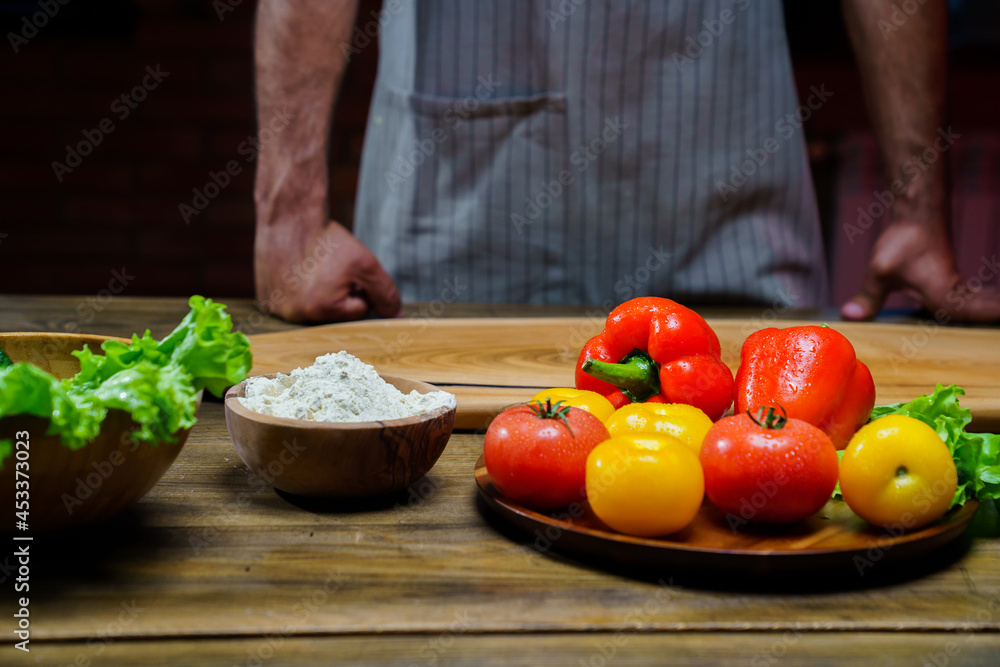a wooden bowl of flour and vegetables on the kitchen table. man in an apron.