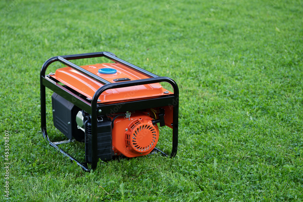 Portable electric generator on the green grass outdoors - obrazy, fototapety, plakaty 