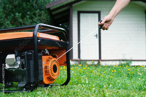 Hand starts a portable electric generator in front of a summer house in summer photo