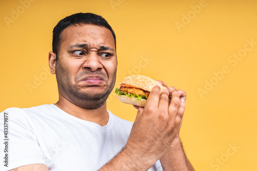 Stop sign. Young african american indian black man eating hamburger isolated over yellow background. Diet concept.