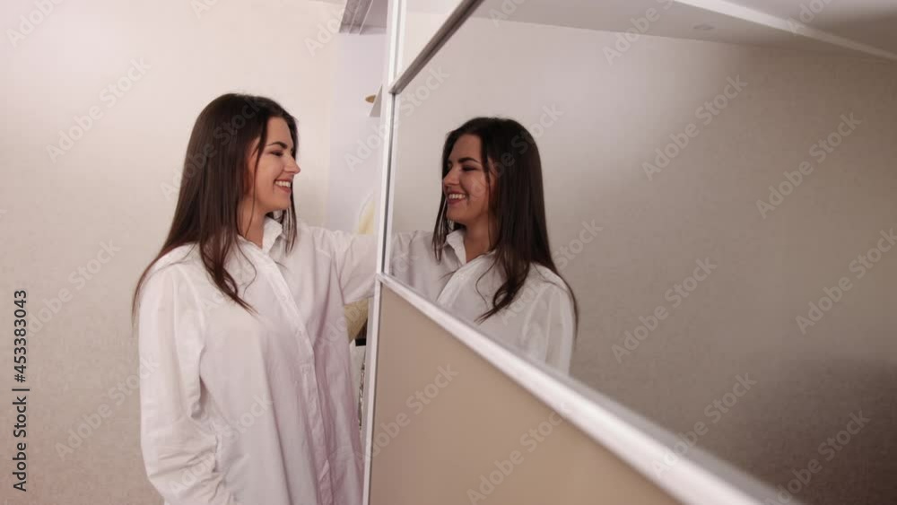 Girl choosing dress in wardrobe, cute young woman in shirt standing in front